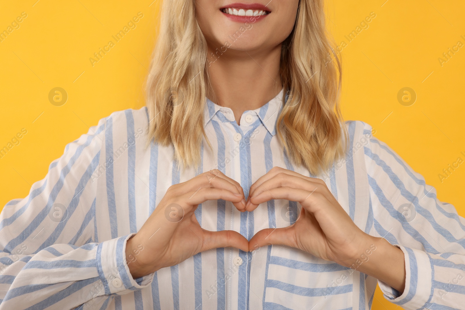 Photo of Happy volunteer making heart with her hands on orange background, closeup