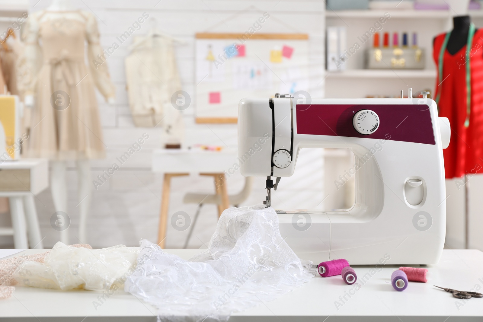 Photo of Modern sewing machine with fabric and bright threads on table in dressmaking workshop