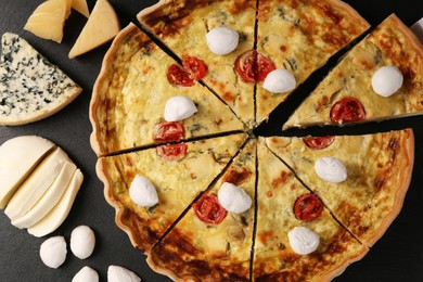 Photo of Delicious homemade cheese quiche and ingredients on black table, flat lay