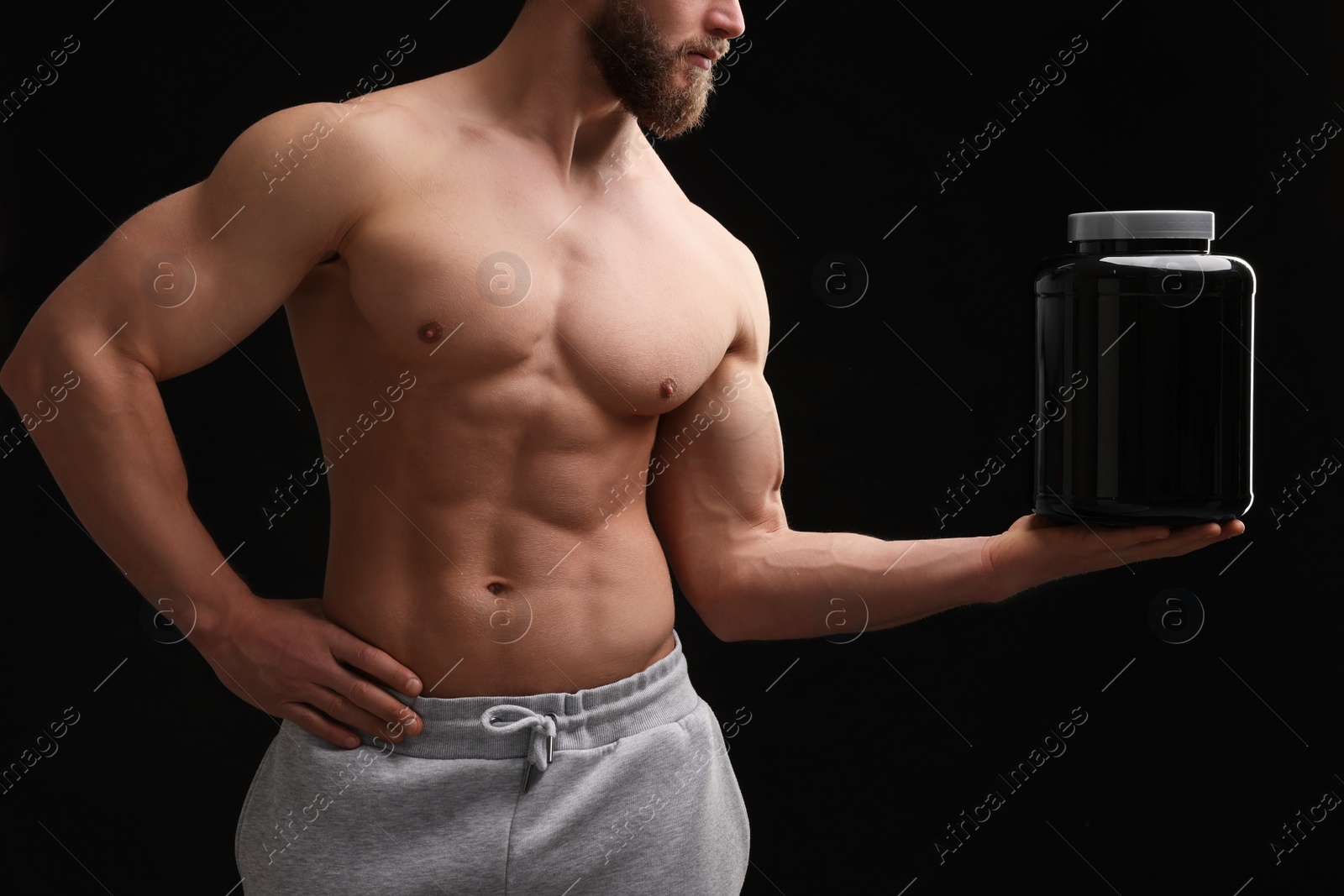 Photo of Young man with muscular body holding jar of protein powder on black background, closeup