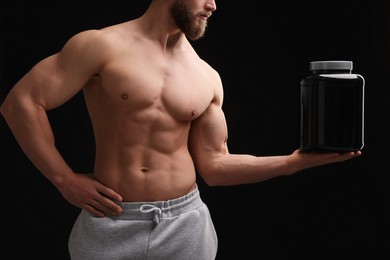 Photo of Young man with muscular body holding jar of protein powder on black background, closeup