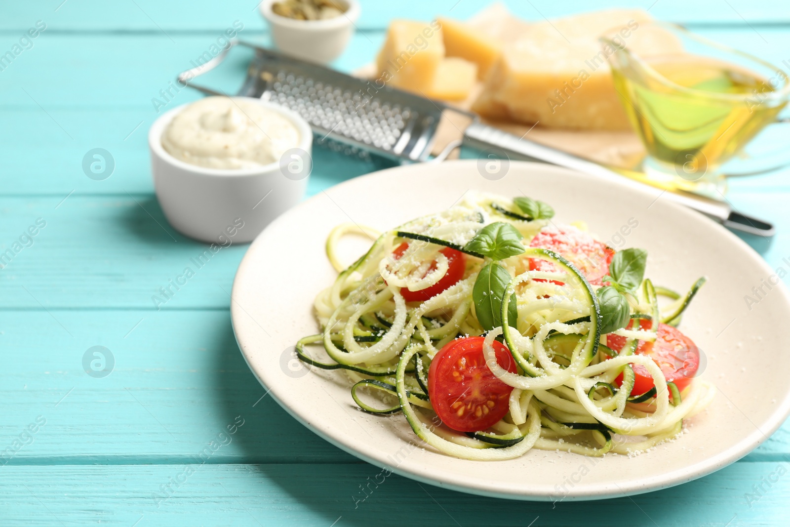 Photo of Delicious zucchini pasta with cherry tomatoes, basil and grated cheese served on light blue wooden table