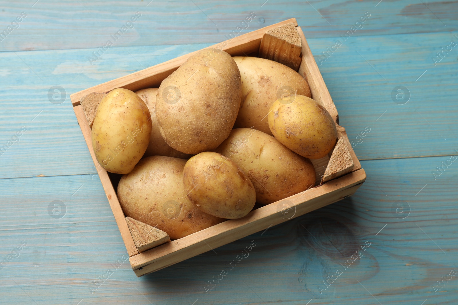 Photo of Raw fresh potatoes in crate on light blue wooden table, top view