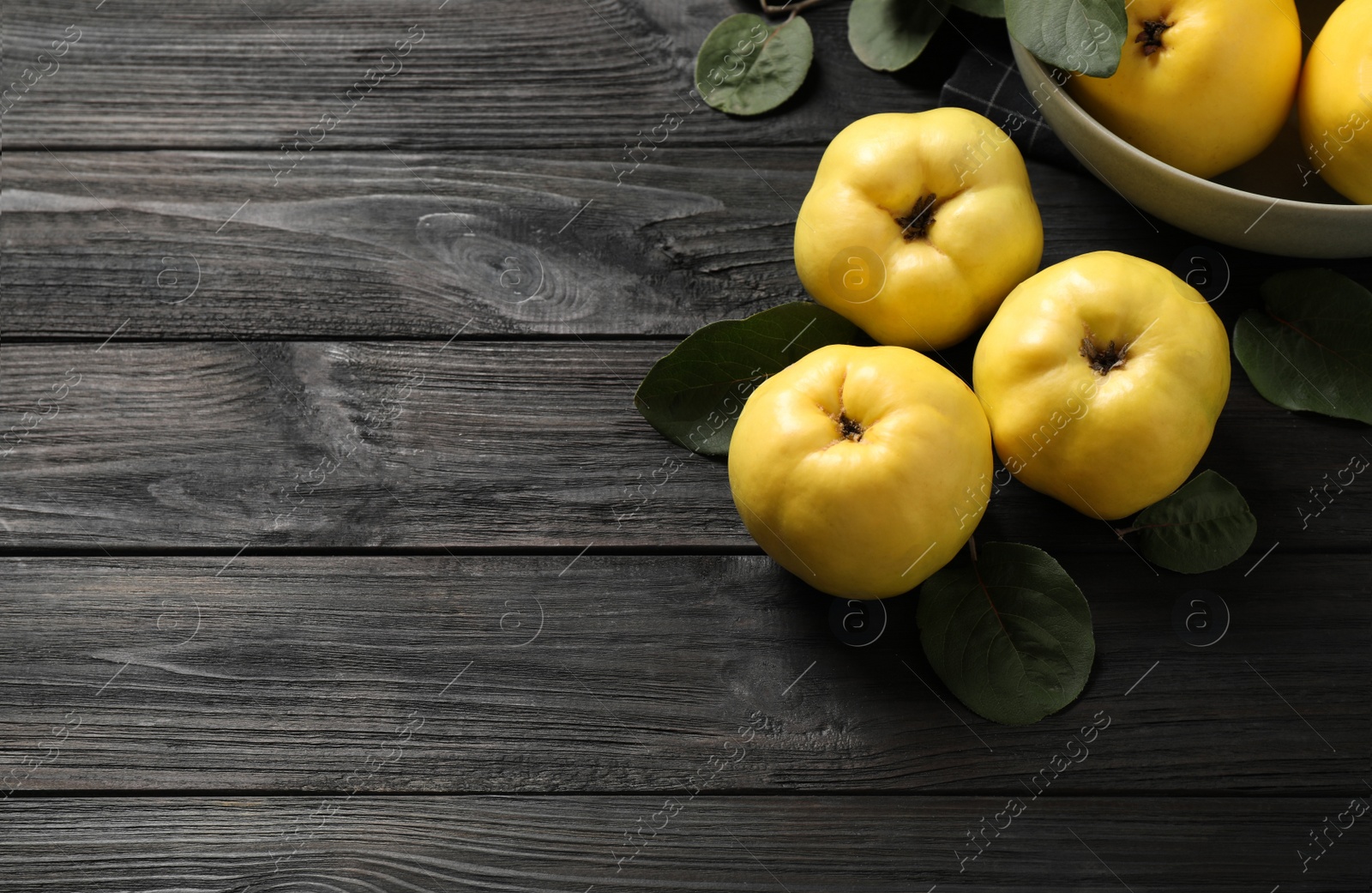 Photo of Fresh ripe organic quinces with leaves on black wooden table, flat lay. Space for text