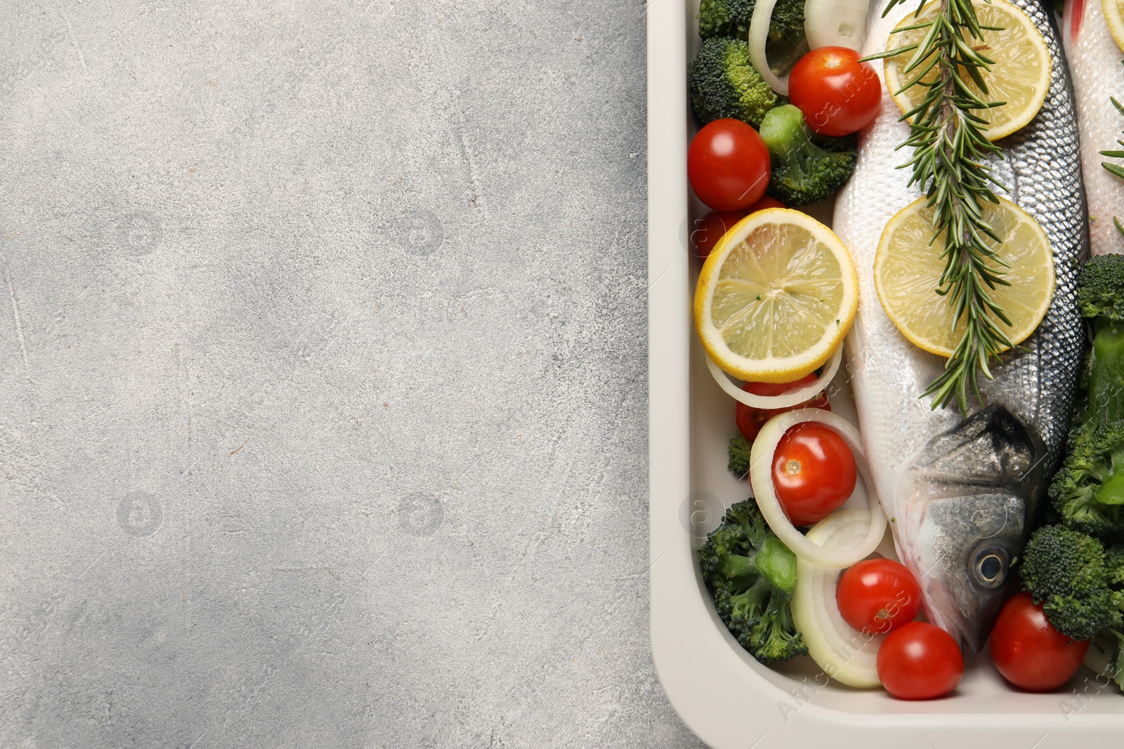 Photo of Raw fish with vegetables and lemon in baking dish on grey textured table, top view. Space for text