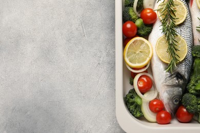 Raw fish with vegetables and lemon in baking dish on grey textured table, top view. Space for text