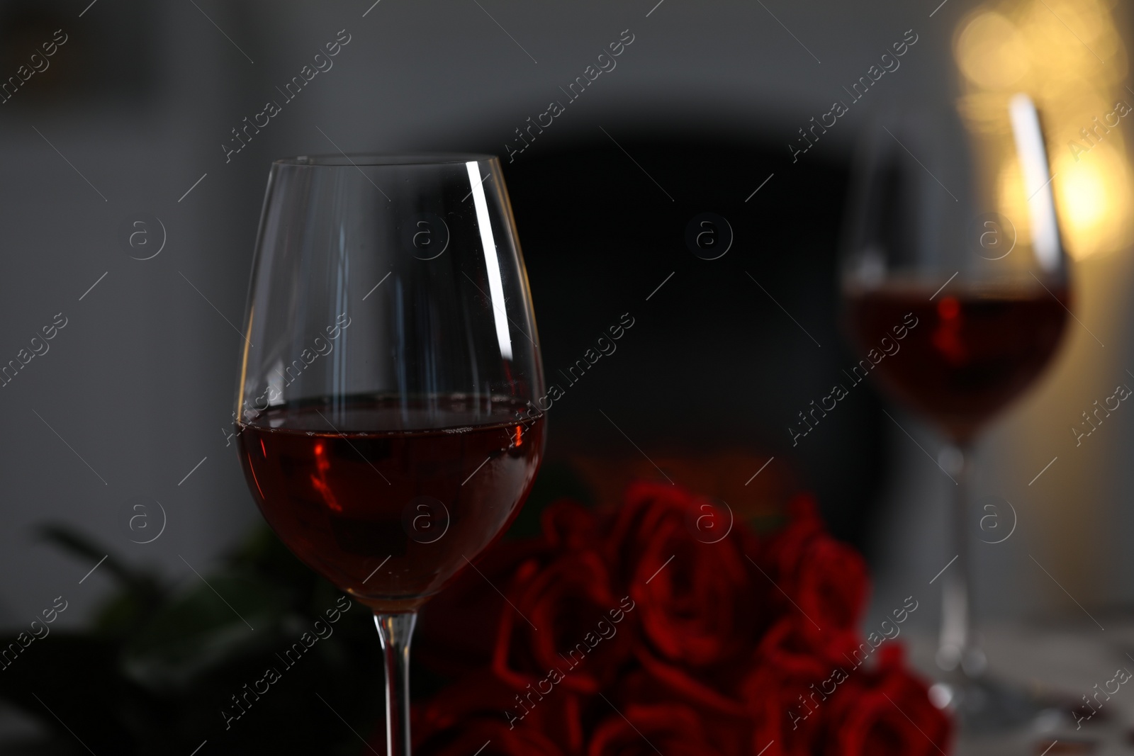 Photo of Glasses of red wine and rose flowers against blurred lights, space for text. Romantic atmosphere