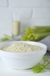 Photo of Natural celery powder in bowl and fresh stalks on white table, closeup