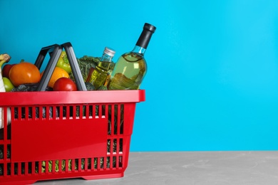 Photo of Shopping basket with grocery products on grey table against light blue background. Space for text