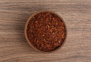 Dry rooibos leaves in bowl on wooden table, top view