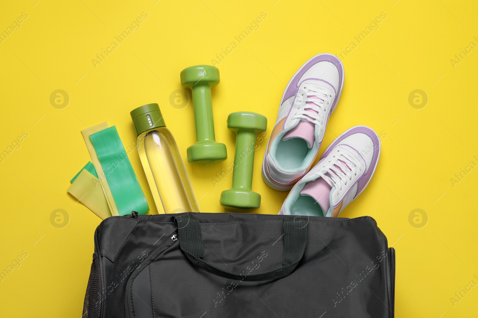 Photo of Gym bag and sports equipment on yellow background, flat lay