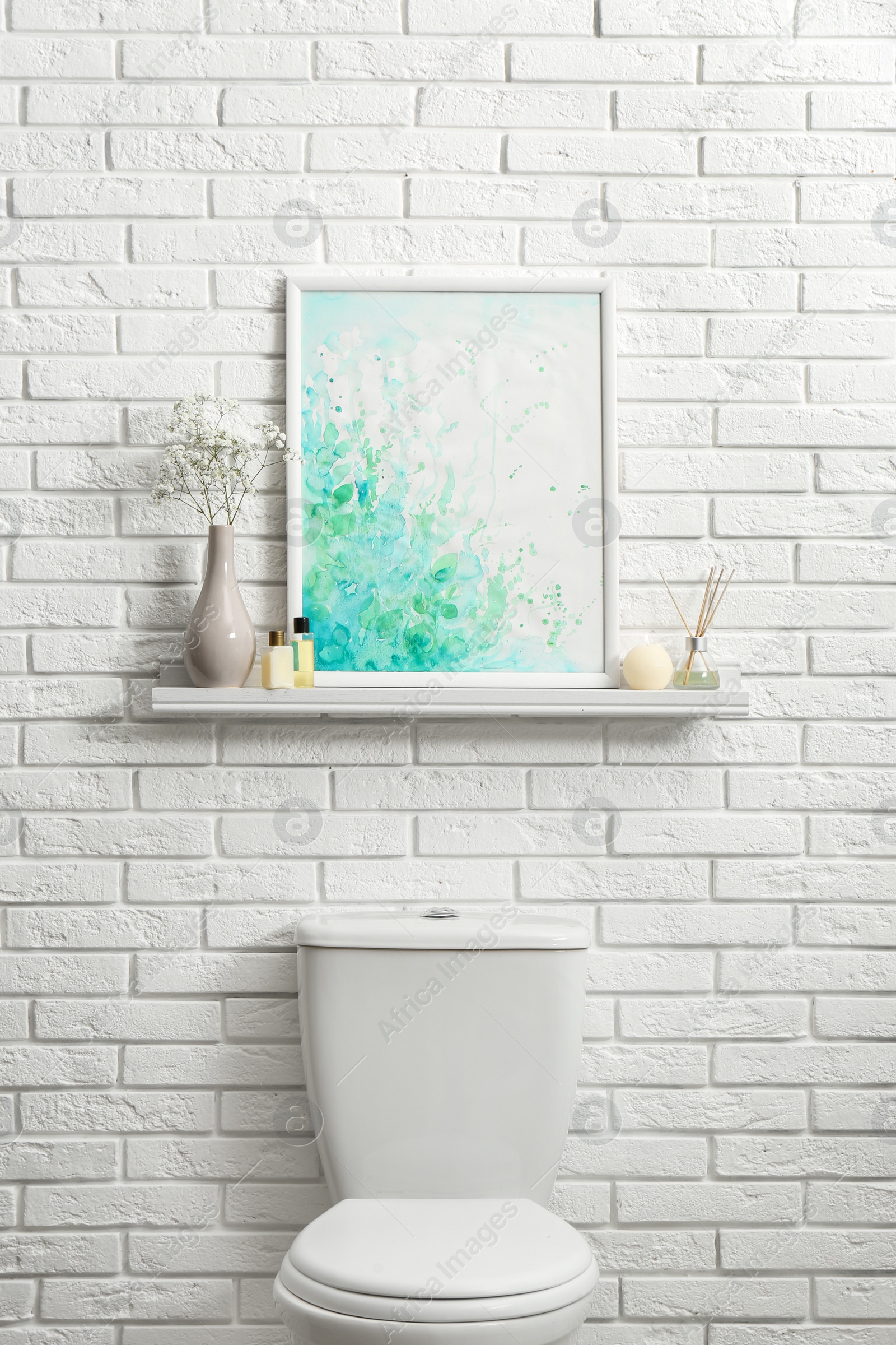 Photo of Shelf with picture on white brick wall above toilet bowl in restroom interior