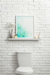 Shelf with picture on white brick wall above toilet bowl in restroom interior