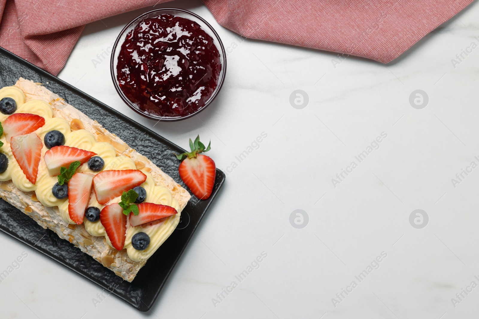 Photo of Tasty meringue roll with jam, cream, strawberry, blueberry and mint on white marble table, flat lay. Space for text