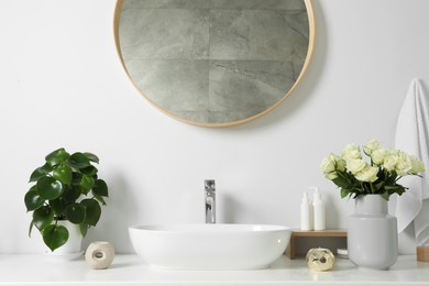 Photo of Vase with beautiful white roses and toiletries near sink in bathroom