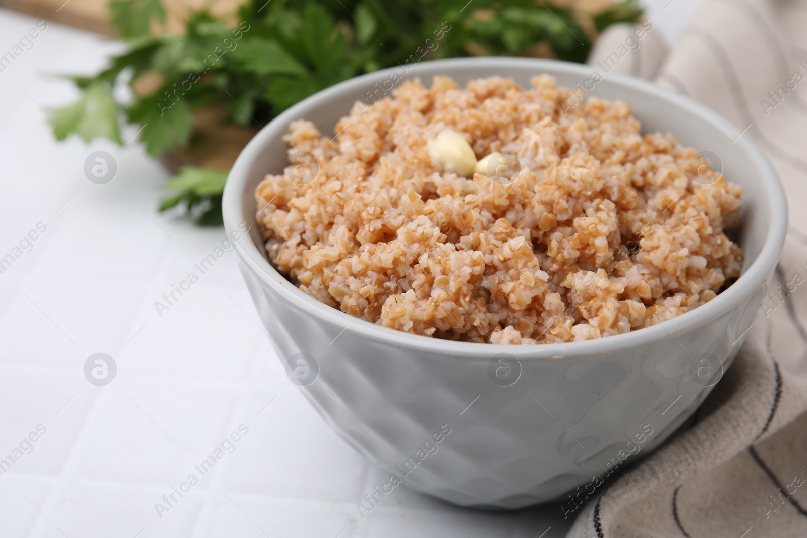 Photo of Tasty wheat porridge with butter in bowl on white tiled table, closeup. Space for text