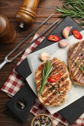 Photo of Delicious grilled pork steaks with spices and meat fork on wooden table, flat lay