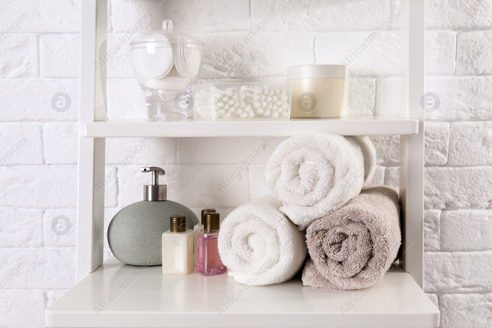 Photo of Shelving unit with clean towels and toiletries near brick wall