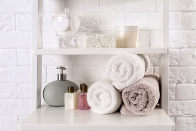 Shelving unit with clean towels and toiletries near brick wall