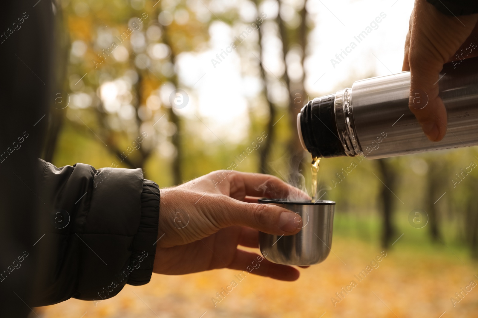 Photo of Man pouring drink from thermos into cap outdoors, closeup