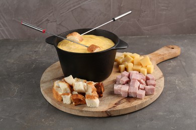 Fondue pot with tasty melted cheese, forks and different snacks on grey table