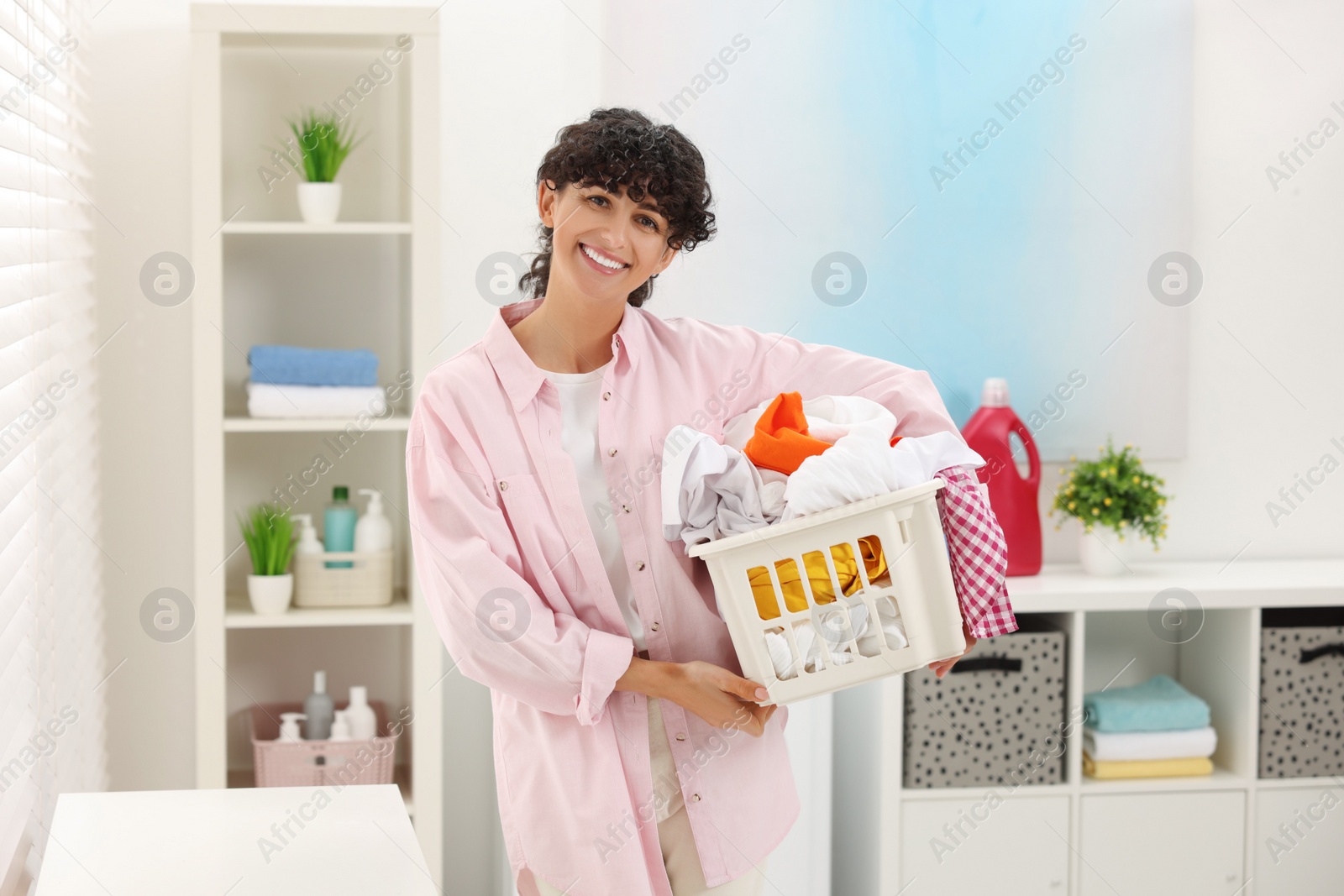 Photo of Happy woman with laundry basket full of clothes indoors