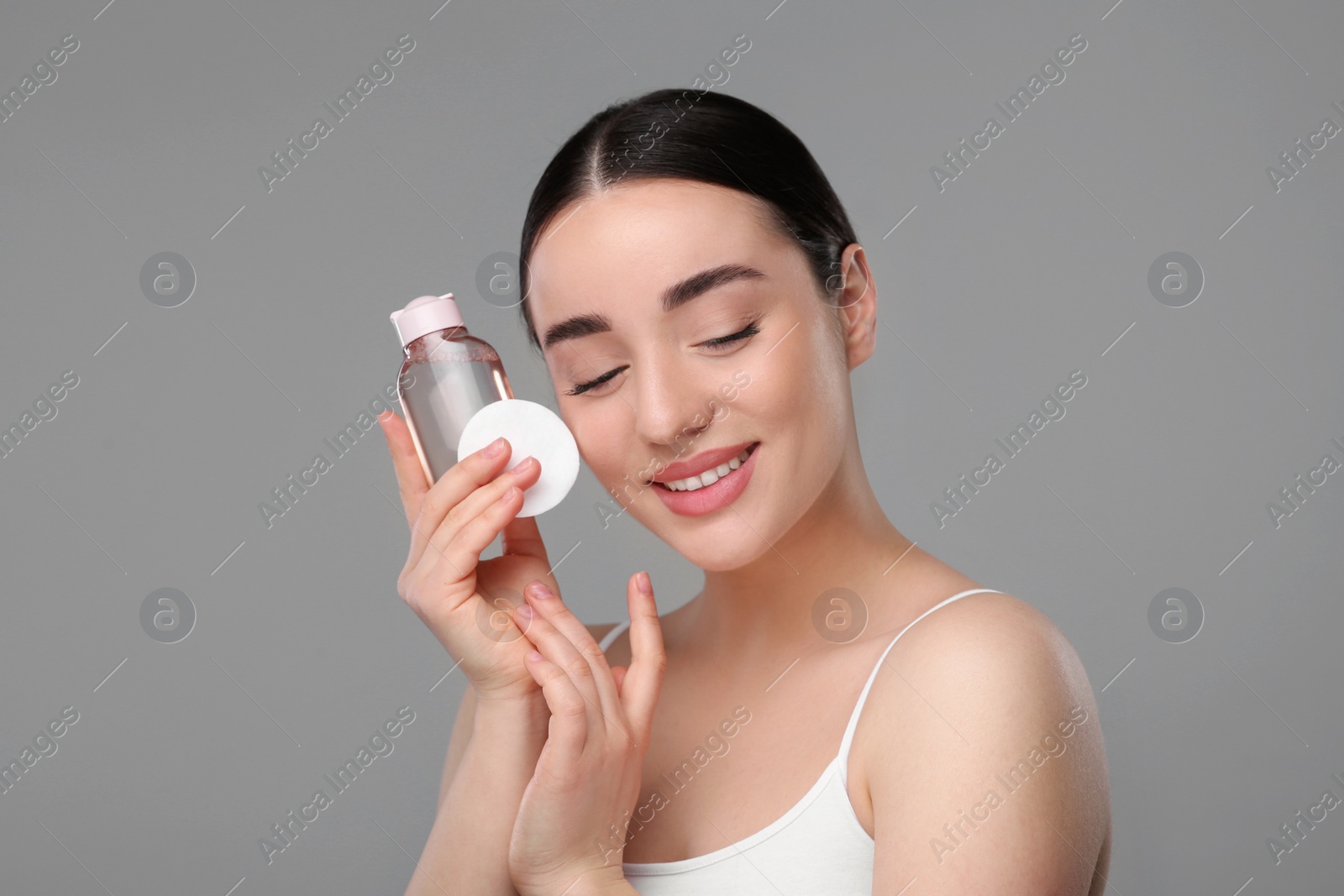 Photo of Beautiful woman with makeup remover and cotton pad on gray background