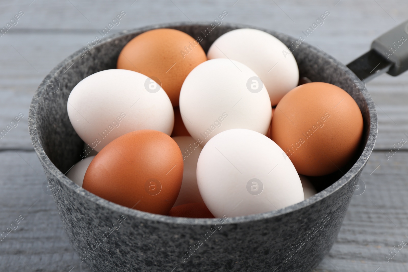 Photo of Unpeeled boiled eggs in saucepan on grey wooden table, closeup