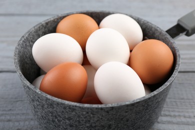 Unpeeled boiled eggs in saucepan on grey wooden table, closeup