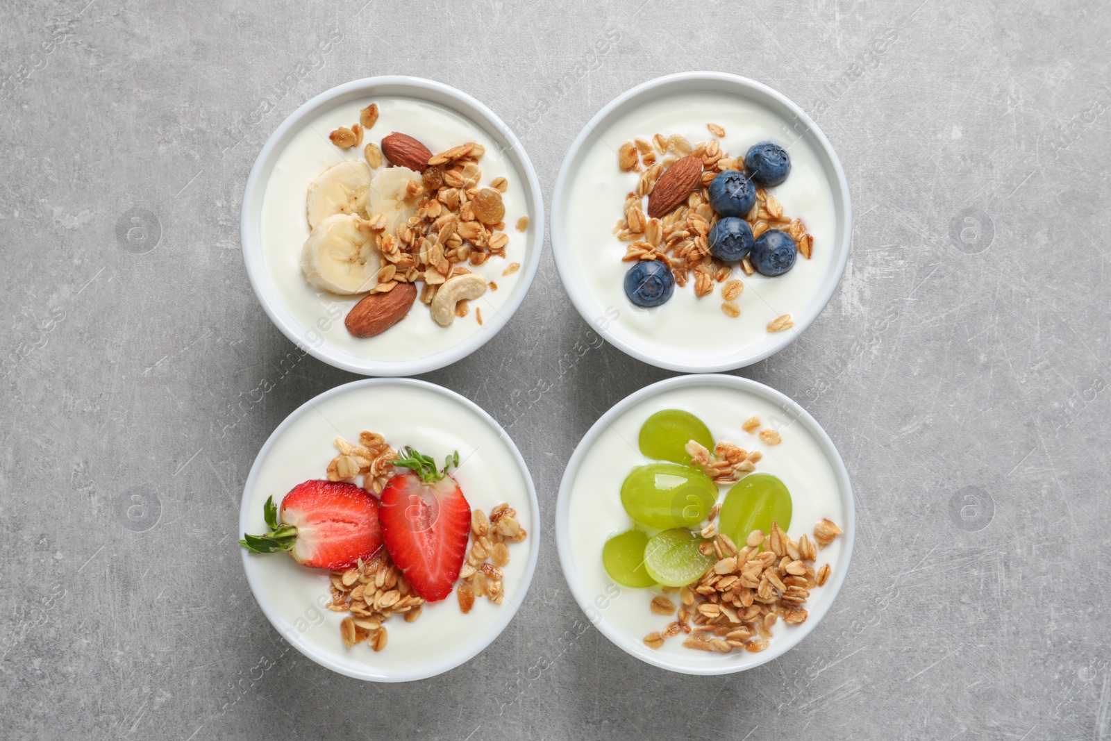 Photo of Bowls with yogurt, granola and different fruits on gray background, top view