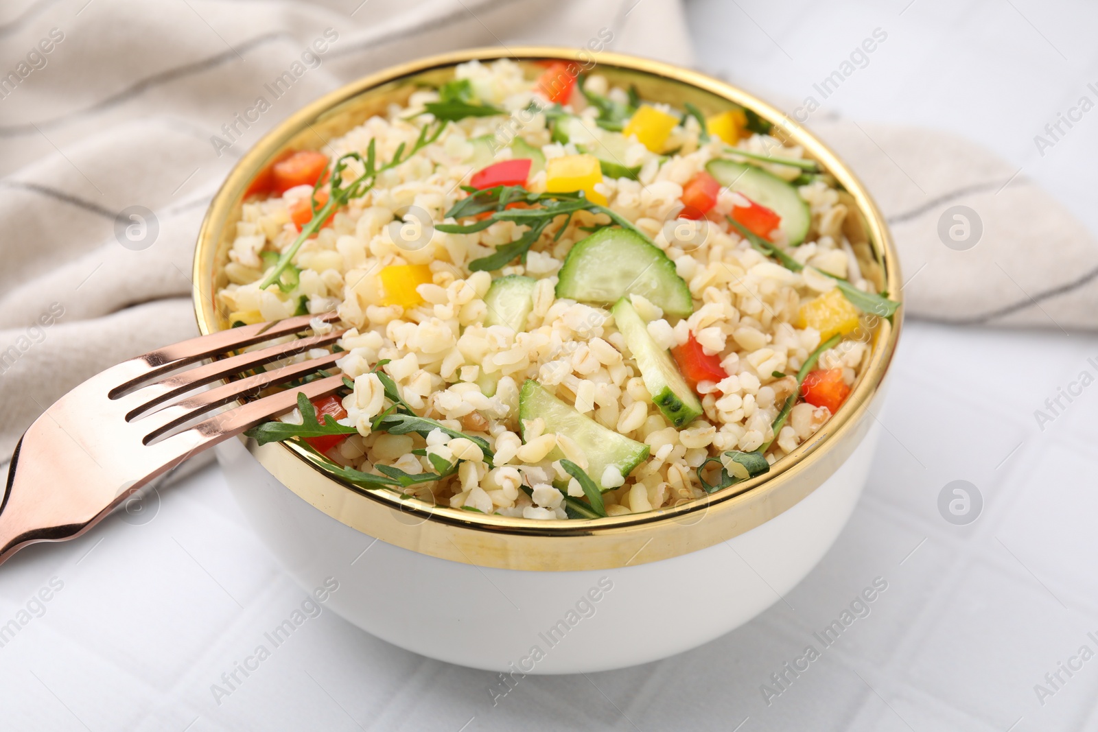 Photo of Cooked bulgur with vegetables in bowl on white tiled table, closeup