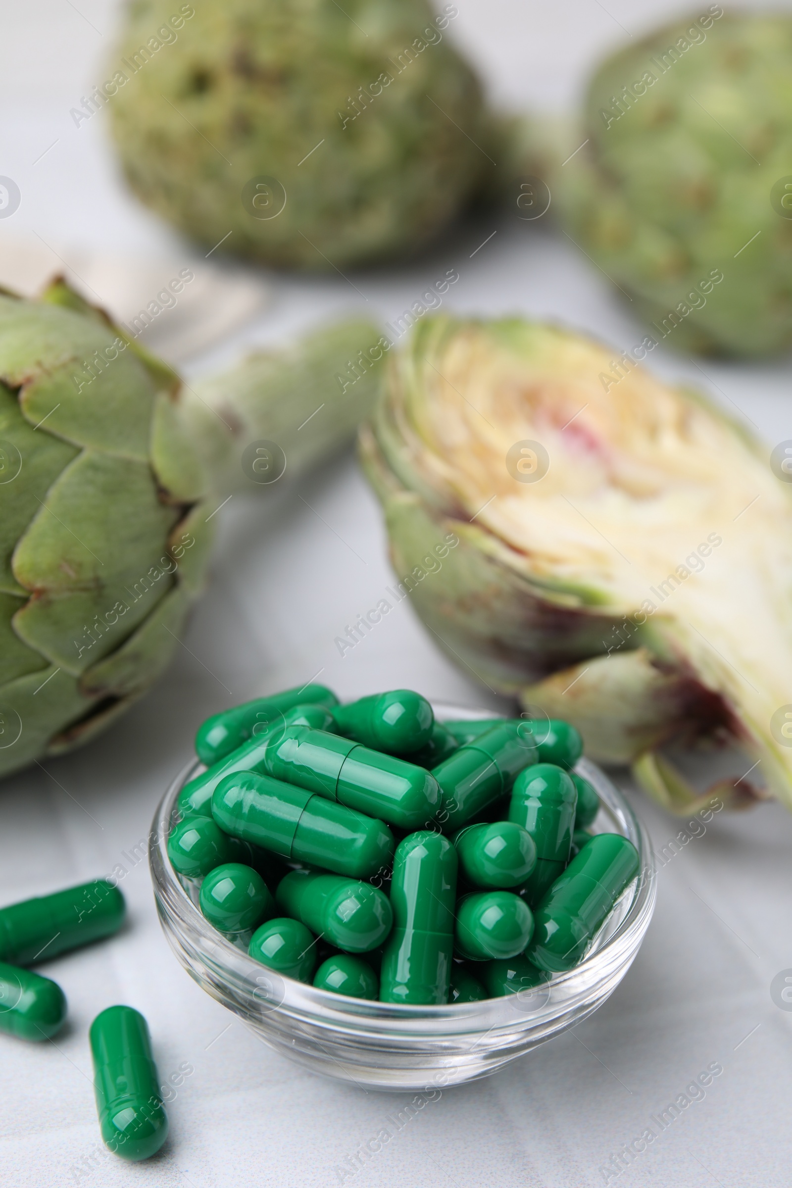 Photo of Bowl with pills and fresh artichokes on white tiled table, closeup