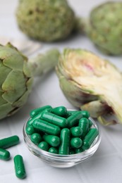 Photo of Bowl with pills and fresh artichokes on white tiled table, closeup