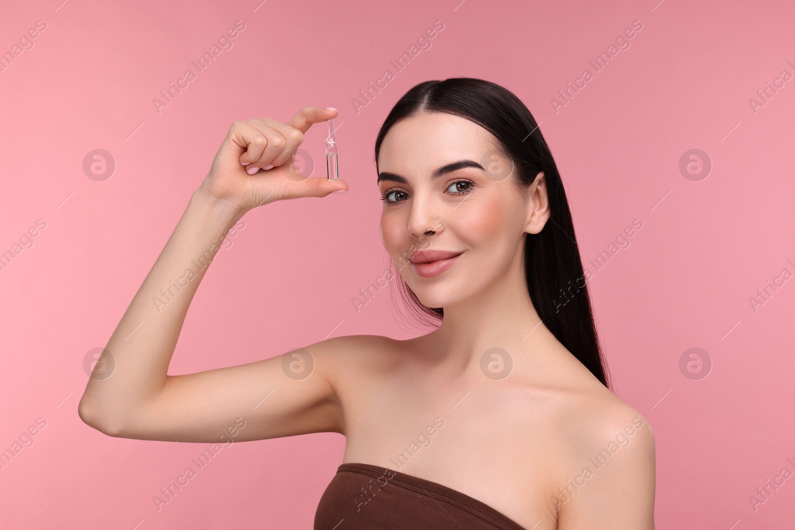 Photo of Beautiful young woman holding skincare ampoule on pink background