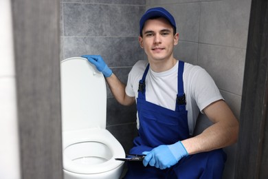 Smiling plumber examining toilet bowl in water closet