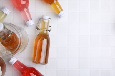 Tasty kombucha in glass bottles on white tiled table, flat lay. Space for text