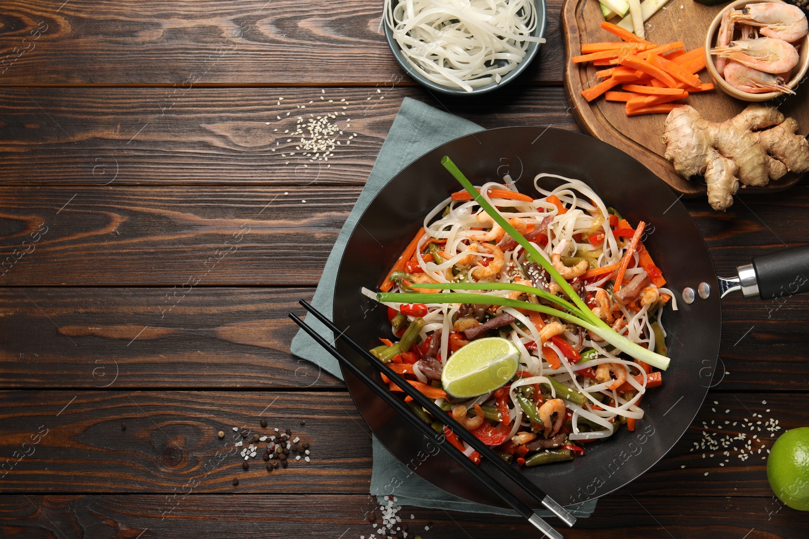 Photo of Shrimp stir fry with noodles and vegetables in wok on wooden table, flat lay. Space for text