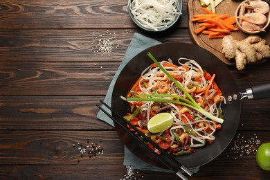 Photo of Shrimp stir fry with noodles and vegetables in wok on wooden table, flat lay. Space for text