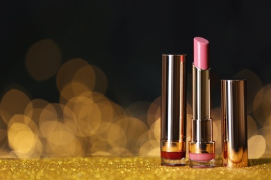 Photo of Bright lipsticks on table with gold glitter against blurred lights, space for text