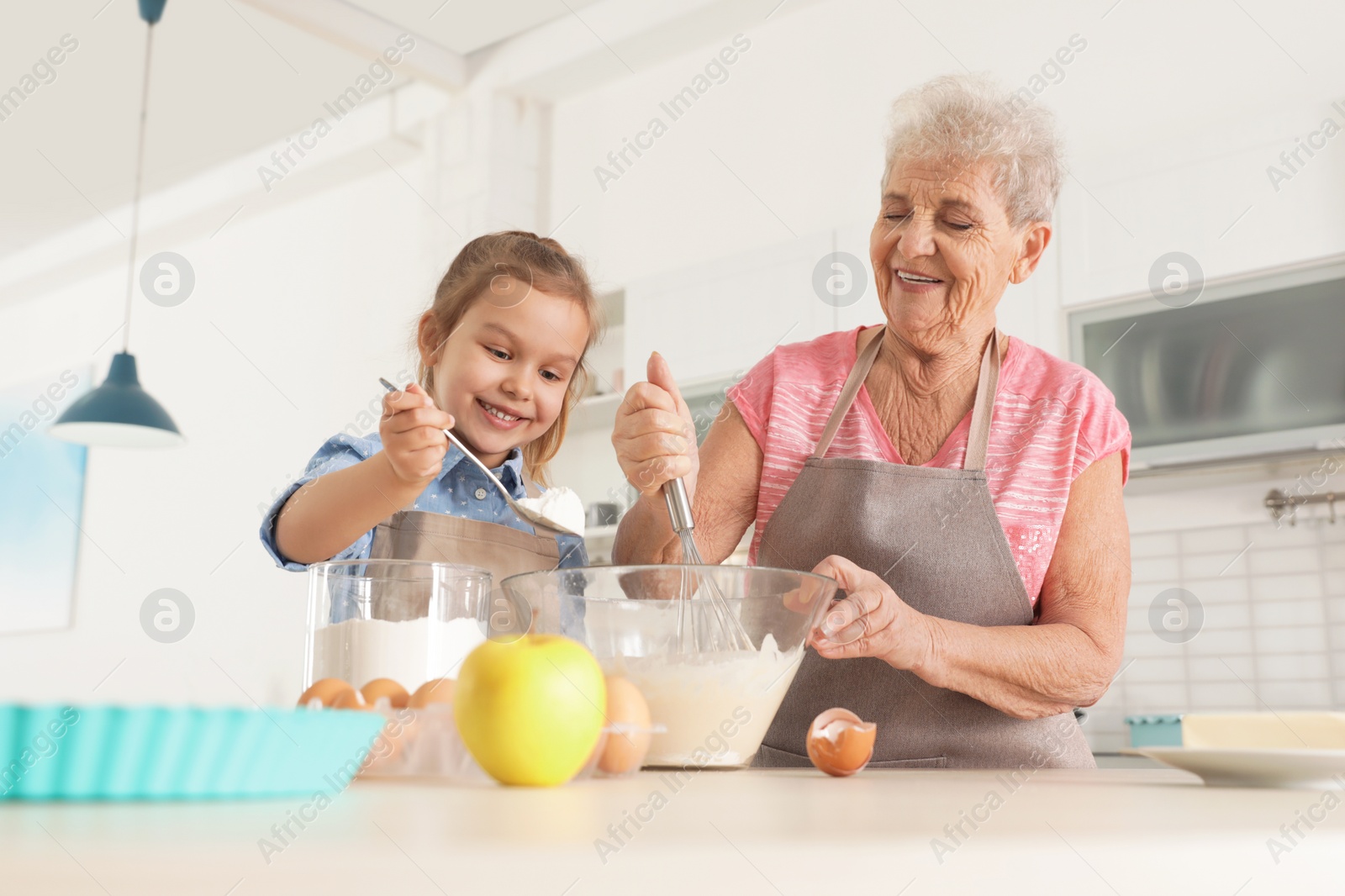 Photo of Cute girl and her grandmother cooking in kitchen