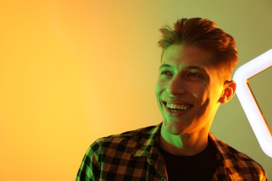 Young man with square lamp on color background in neon lights. Space for text