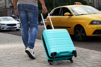 Man with suitcase going to taxi car outdoors, closeup