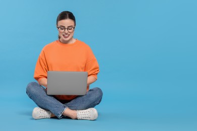 Photo of Happy woman in glasses using laptop on light blue background. Space for text