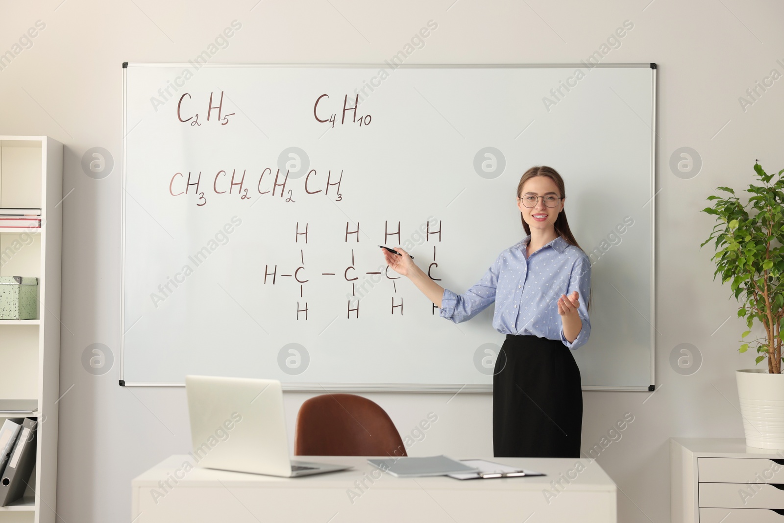 Photo of Young chemistry teacher giving lesson near whiteboard in classroom