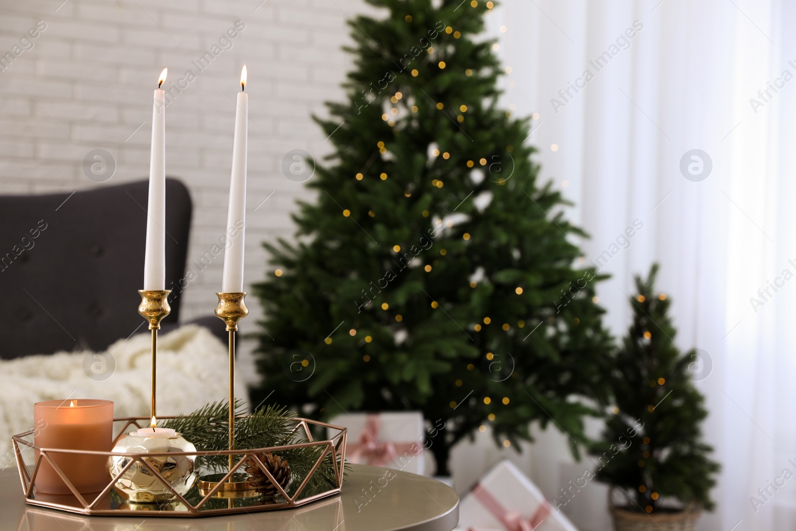 Photo of Burning candles and fir branch on table indoors, space for text. Christmas celebration