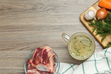 Photo of Glass cup with delicious bone broth and ingredients on wooden table, flat lay. Space for text