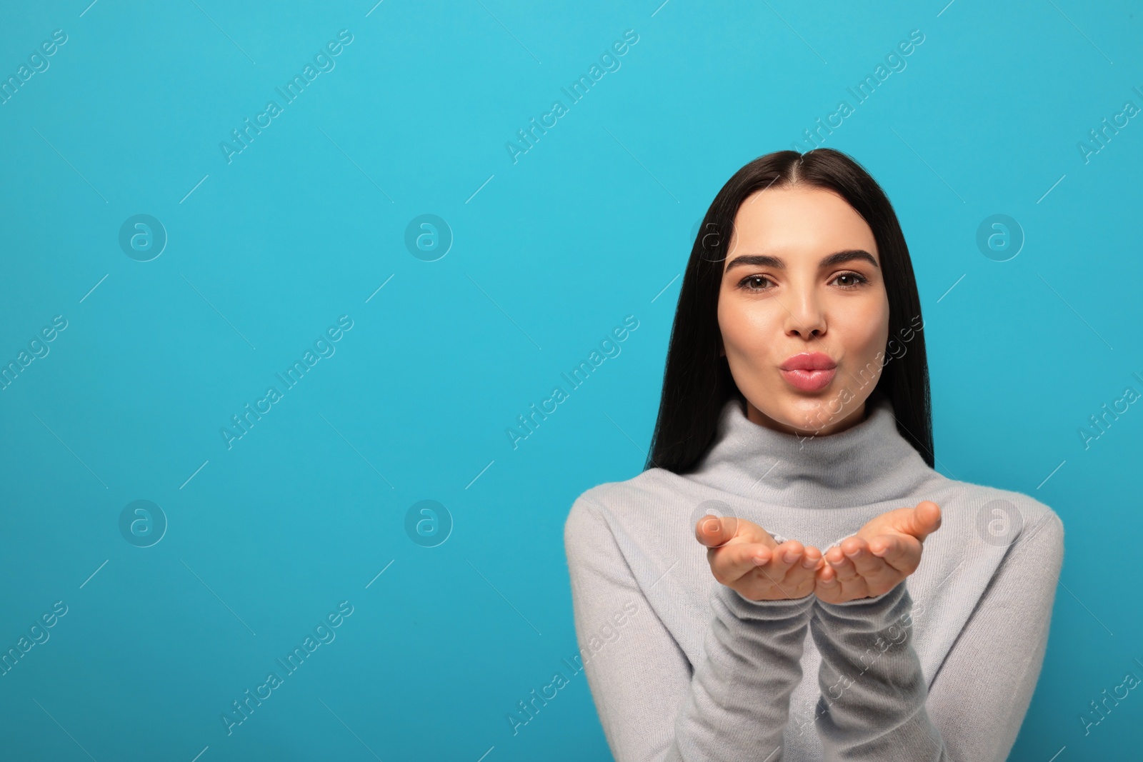 Photo of Beautiful young woman blowing kiss on light blue background. Space for text