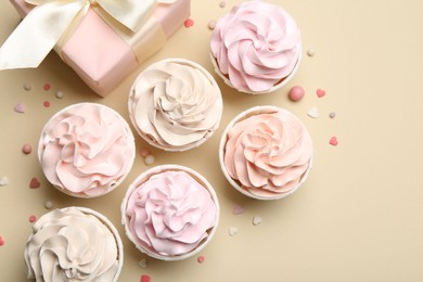 Photo of Delicious birthday cupcakes, gift box and sprinkles on beige background, flat lay. Space for text