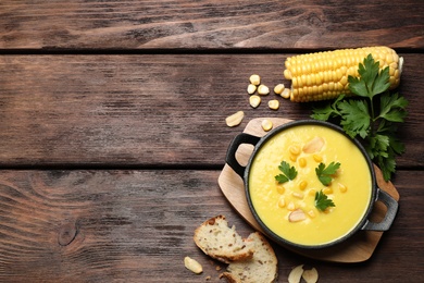 Photo of Delicious creamy corn soup, bread and cob on wooden table, flat lay. Space for text