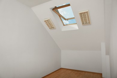 Photo of Light spacious attic room with roof window on slanted ceiling